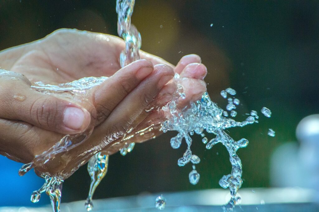 A person's hands cupped under a stream of clear, clean drinking water, symbolizing the importance of water purity and disease prevention.