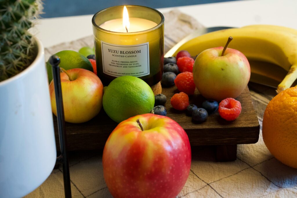A vibrant assortment of fresh fruits, including apples, blueberries, and bananas, next to a lit candle, illustrating the careful consideration needed for how to break a fast safely, with some fruits requiring more caution than others.