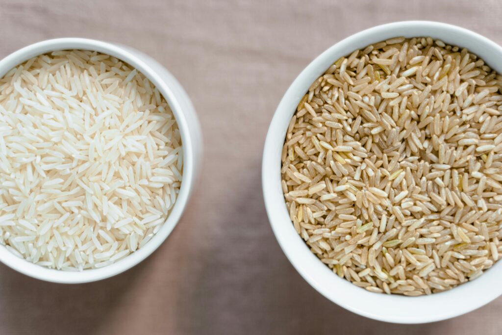 Top-down view comparing uncooked white polished rice and natural brown rice in bowls, highlighting the visual difference and the nutritional choice that impacts polished rice health risks.
