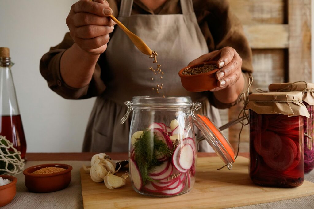 The process of preparing and taking herbs like dill and garlic to add to a jar of cucumbers for homemade fermentation.