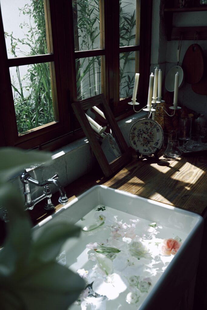 Rustic kitchen sink with sunlit water and floating flowers, symbolizing the soothing tradition of curative baths at home.