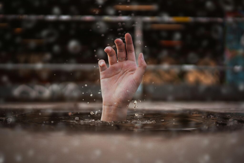 pexels-photo-3651632-3651632 A single hand emerging from water during heavy rain, symbolizing the urgent need for first aid for drowning victims and quick rescue response.