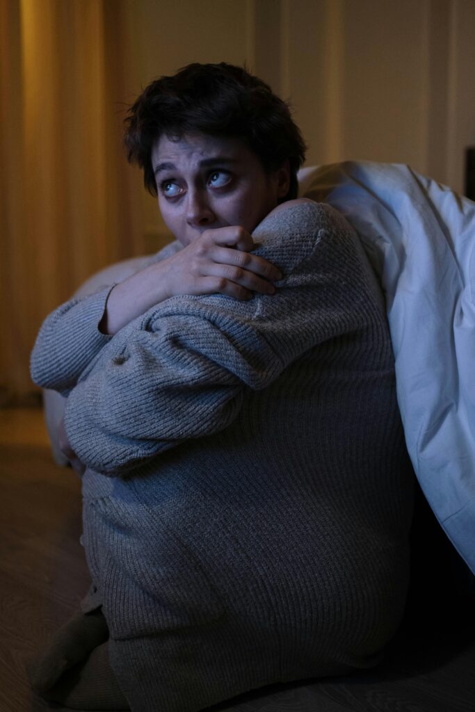 Anxious woman sitting alone in a dimly lit room at night, symbolizing nervousness in women caused by stress, poor sleep, and lifestyle imbalances.
