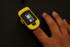 Close-up of a yellow pulse oximeter on a finger measuring oxygen saturation for interpreting signs and symptoms at home