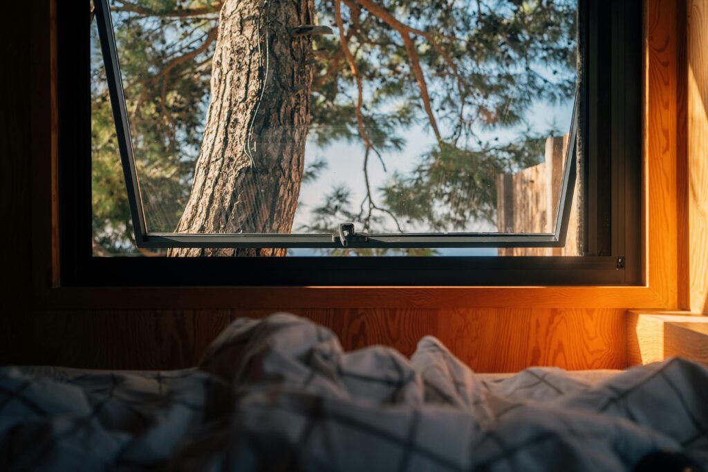 Fresh air through an open window transforms sleep quality—nature's simplest sleep aid. Open bedroom window with fresh morning light streaming in, symbolizing natural sleep hygiene and healthy air circulation.