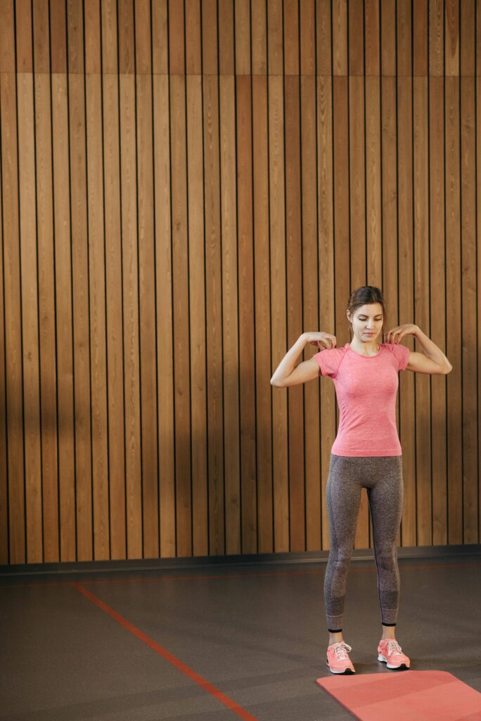 Young woman in sportswear doing shoulder rotations indoors on a yoga mat. Shoulder roll demonstration—key joint mobility exercises for relieving tension and stiffness.