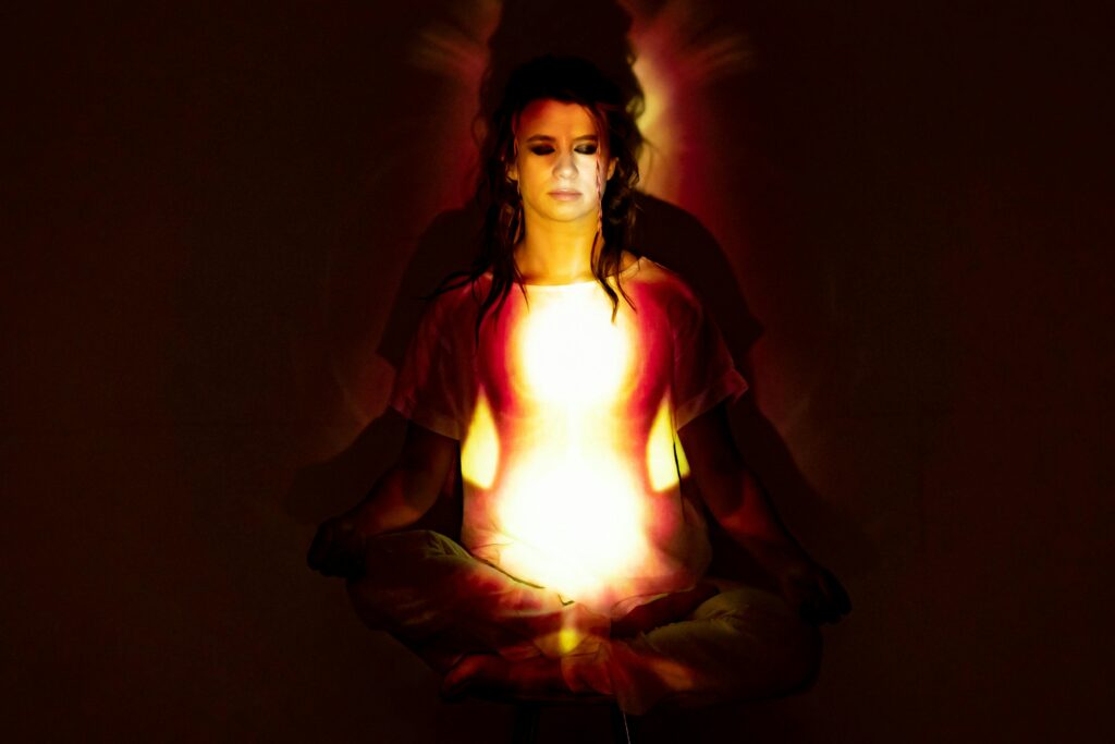 In stillness, we align with the harmony of the laws of the universe. This meditative state allows consciousness to transcend the illusion of a separate self, connecting with the wider cosmic intelligence and activating our inherent potential for spiritual evolution. A woman in deep meditation, her serene focus demonstrating the practical application of the laws of the universe as a radiant aura of spiritual energy surrounds her.