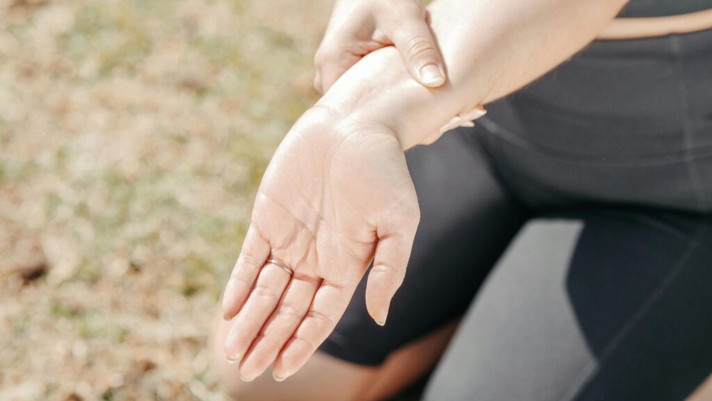 Person gripping wrist in pain, highlighting injury and support outdoors. Wrist pain from stiffness—joint mobility exercises prevent injury and restore flexibility.