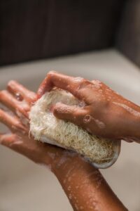 .Hands scrubbing with a loofah in a bath setting, focusing on personal hygiene. Hands scrubbing with a loofah in a bath, highlighting skin detoxification through bathing for improved hygiene, circulation, and overall health